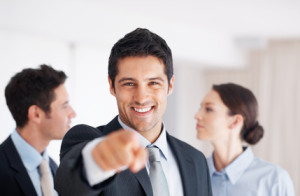 Smiling business man pointing at you with colleagues in background